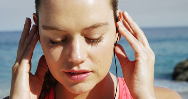 Close-up of fit woman putting earphones in her ear before jogging on the beach