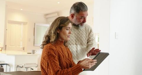 Mature couple using tablet in cozy home living room, planning finances and travel together