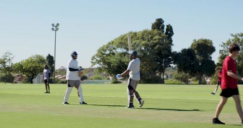 Two batsmen walking off pitch after partnership on sunny community cricket field