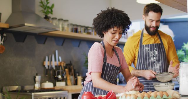 Image of happy diverse couple in aprons talking and baking together in kitchen, with copy space. Happiness, inclusivity, free time, togetherness and domestic life.