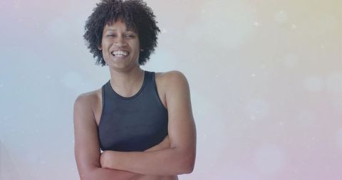 Confident black woman standing with arms crossed smiling in pastel bokeh backdrop wellness