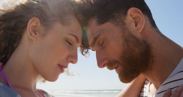 Loving couple standing close on a beach, touching foreheads. Sunlight illuminating their faces creates a warm, intimate moment. Perfect for advertisements promoting travel, vacation destinations, romantic getaways, love-themed products, or relationship advice content.