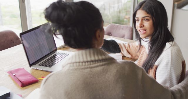 Image of focused biracial women working from home with laptop. Friendship, working from home and spending time together.