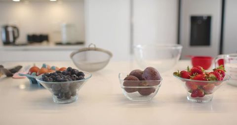 Three glass bowls displaying blueberries, plums, strawberries on modern kitchen countertop