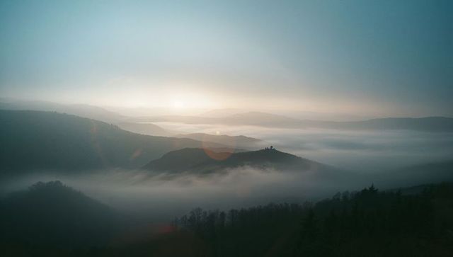 Misty hills in dawn light with rising sun and mist-filled valleys