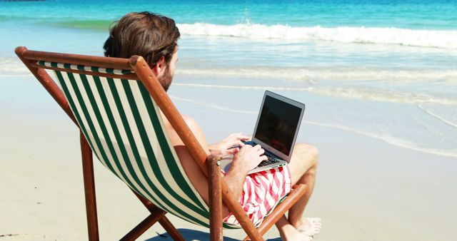Man sitting on armchair using laptop at beach 4k