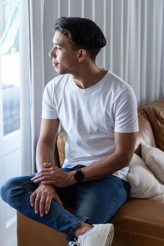 Young african american man sitting on leather sofa looking out window in white t-shirt