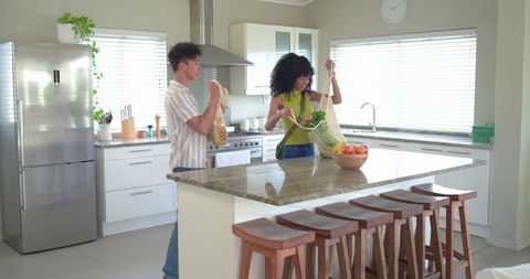 Multiracial couple unpacking groceries in modern bright kitchen placing apples on island