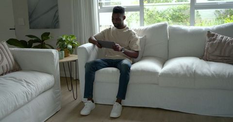African american man sitting on sofa using tablet in modern living room
