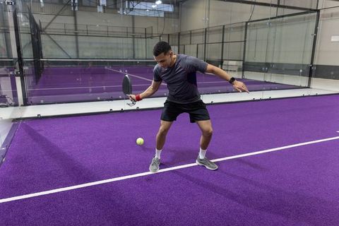 Male padel player hitting forehand on vibrant purple indoor court showing agility