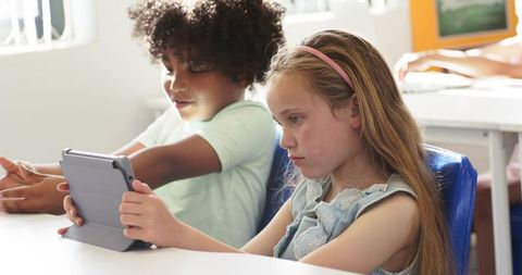 Children sharing tablet for collaborative learning in bright classroom