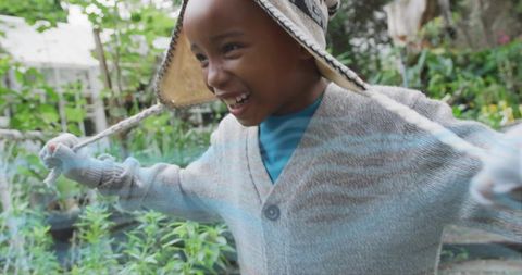 Joyful child laughing with arms outstretched in cozy knit hat and sweater in garden