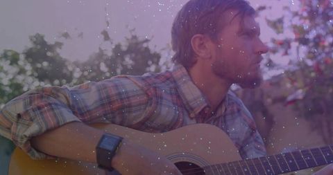 Man Playing Guitar Outdoors in Relaxed Garden Atmosphere with Sparkles