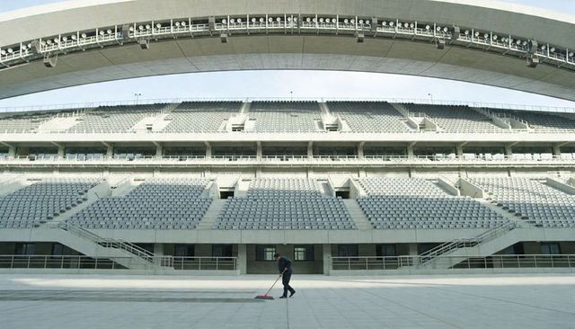 Solo janitor sweeping empty multi-level stadium floor under curved concrete canopy routine