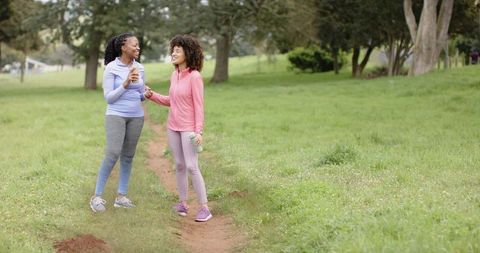 Smiling diverse women chatting on park trail after workout holding water bottles