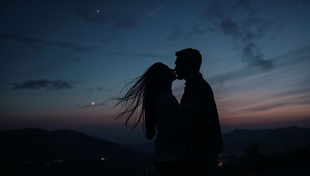 Couple kissing silhouetted against twilight sky on hilltop