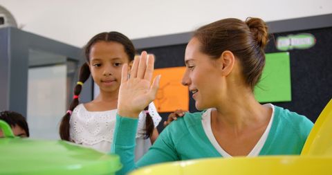 Caucasian teacher high-fiving schoolgirl in classroom