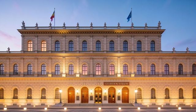 Neoclassical museum facade glowing at dusk with arched windows, five wooden doors and flags