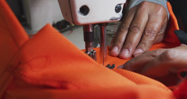 Hands sewing orange fabric on industrial sewing machine demonstrates precision and craftsmanship in textile work. Excellent for illustrating manual work in the textile industry, showcasing professional sewing techniques, or presenting themes of craftsmanship and garment manufacturing.
