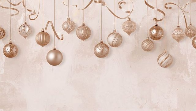 Hanging rose gold holiday baubles and curled ribbons decorating blush textured backdrop