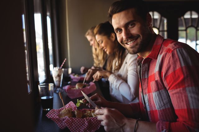 Group of friends enjoying burgers and drinks at a restaurant. Perfect for illustrating social gatherings, dining out, and casual lifestyle themes. Ideal for use in advertisements, blog posts, and social media content related to food, friendship, and leisure activities.