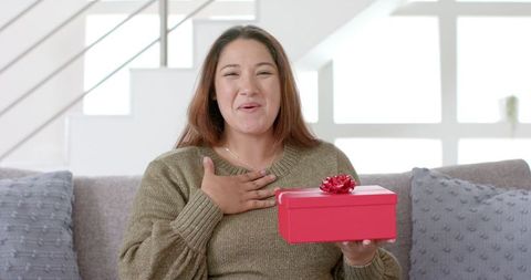 Joyful woman holding gift box during video call at home