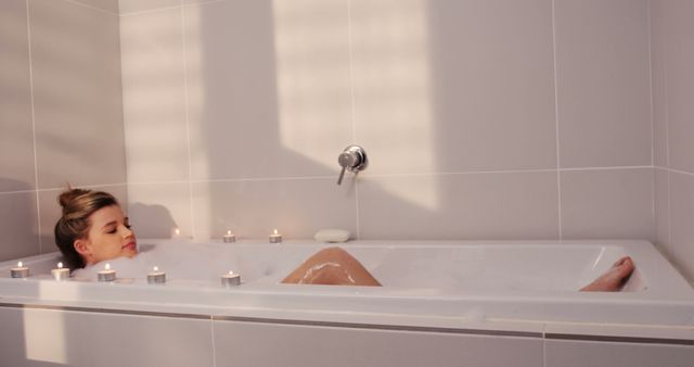 This image portrays a woman enjoying a relaxing bubble bath with candlelight in a modern, tiled bathroom. Perfect for illustrating concepts such as self-care, relaxation, home spa, and peaceful moments. Suitable for use in articles, blogs, or advertisements related to wellness, lifestyle, interior design, and self-pampering routines.