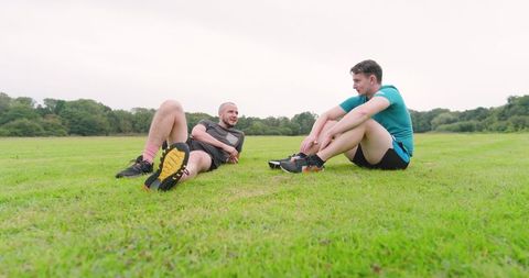 Friends Relaxing on Grass in Park after Jogging Workout