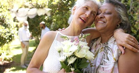 Joyful Senior Bride with Bridesmaid Hugging Outdoors