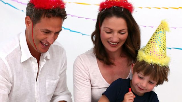 Parents enjoy quality time with their son during his birthday celebration, wearing festive hats and sharing moments of joy. Perfect for use in advertisements, parenting magazines, birthday invitations, and social media posts highlighting family moments and celebrations.