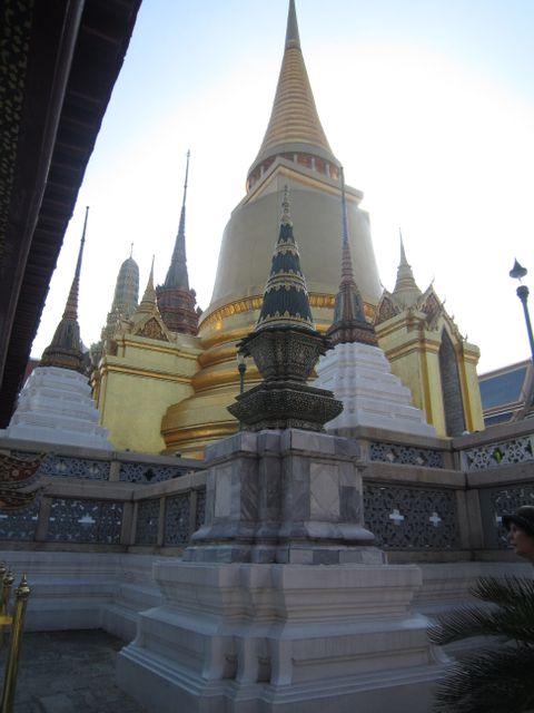 Golden temple structures with multiple spires captured in Grand Palace complex, Bangkok. Reflective gold emphasizing cultural and historic significance. Perfect for travel blogs, tourism websites, educational articles on Asian architecture, and media on Thailand’s historic landmarks and religious heritage.