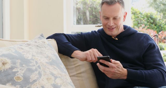 A middle-aged man enjoys his smartphone indoors, epitomizing contemporary digital leisure. - Download Free Stock Photos Pikwizard.com