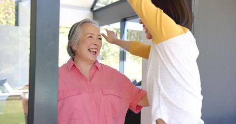 Senior asian mother and daughter greeting with open arms at sliding door