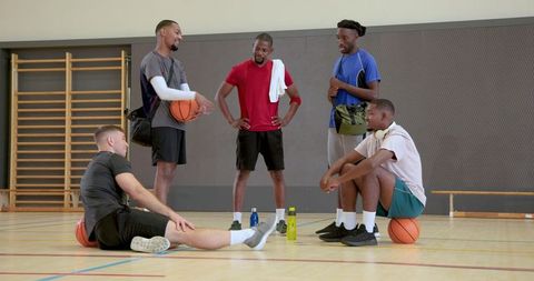 Diverse basketball teammates chatting, resting, and preparing on indoor gym court