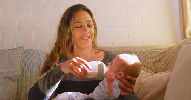 Smiling Mother Feeding Newborn Baby with Bottle on Sofa at Home - Download Free Stock Images Pikwizard.com