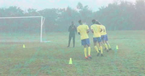 Misty soccer training session with coach timing cone sprint drills near goal on wet turf