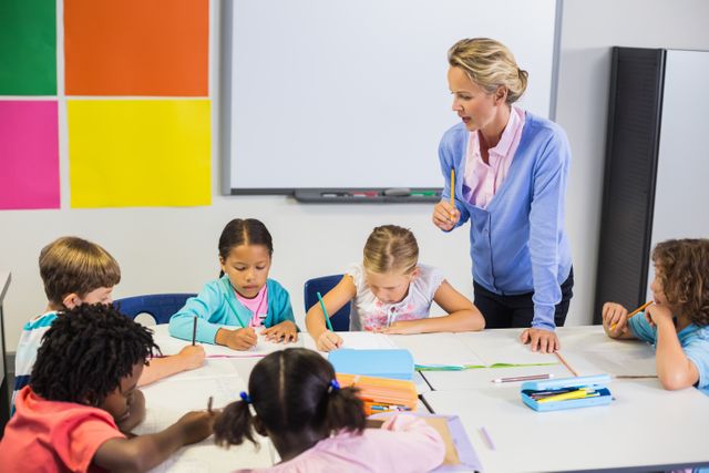 Teacher assisting a group of young students with their homework in a classroom setting. Ideal for educational content, school brochures, teaching resources, and articles on childhood education and learning environments.