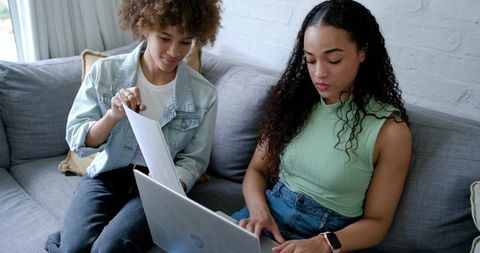 African american women collaborating on laptop and documents on couch at home