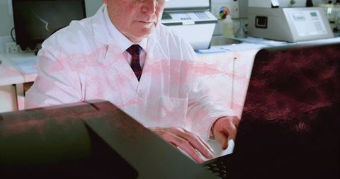 Senior lab technician typing on laptop in print room with copier and printer equipment