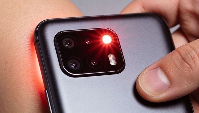 Macro closeup smartphone rear triple camera with red led flash flaring on bare skin and fingertip