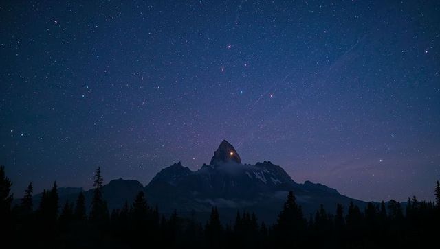 Jagged mountain peak glowing under starry night with summit light and conifer silhouette