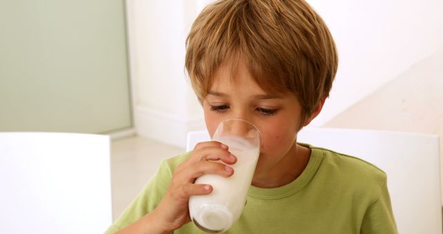 Boy enjoys drinking glass of milk in kitchen. Great for healthy eating, child nutrition, and family lifestyle promotions. Can be used for articles related to child health, dairy products, and balanced diets.