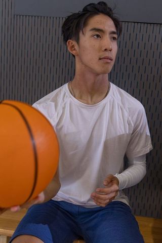 Asian athlete sitting on bench catching basketball wearing compression sleeve focused gym