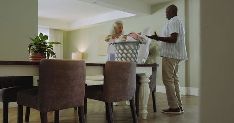 Diverse senior couple folding laundry together at home