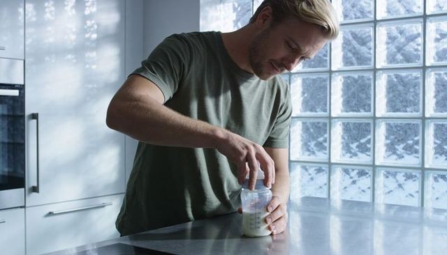 Father preparing baby bottle on stainless countertop in bright modern kitchen