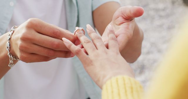 Close-up of person putting engagement ring on partner's finger. Perfect for illustrating marriage proposals, romantic moments, or articles about engagements and weddings.