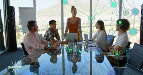 Woman presenting to team around glass conference table with digital network overlay and laptops