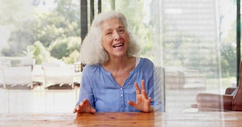 Senior woman gesturing while talking at sunlit patio table, candid lifestyle portrait