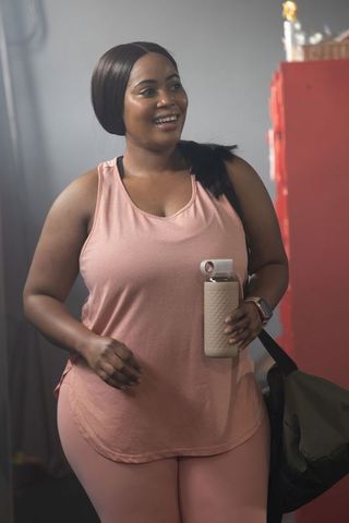 African-american woman smiling in pink activewear holding textured bottle and gym bag