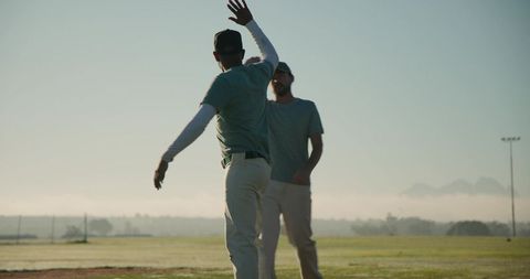 Two teammates celebrating with high five on baseball field at dawn with misty mountains